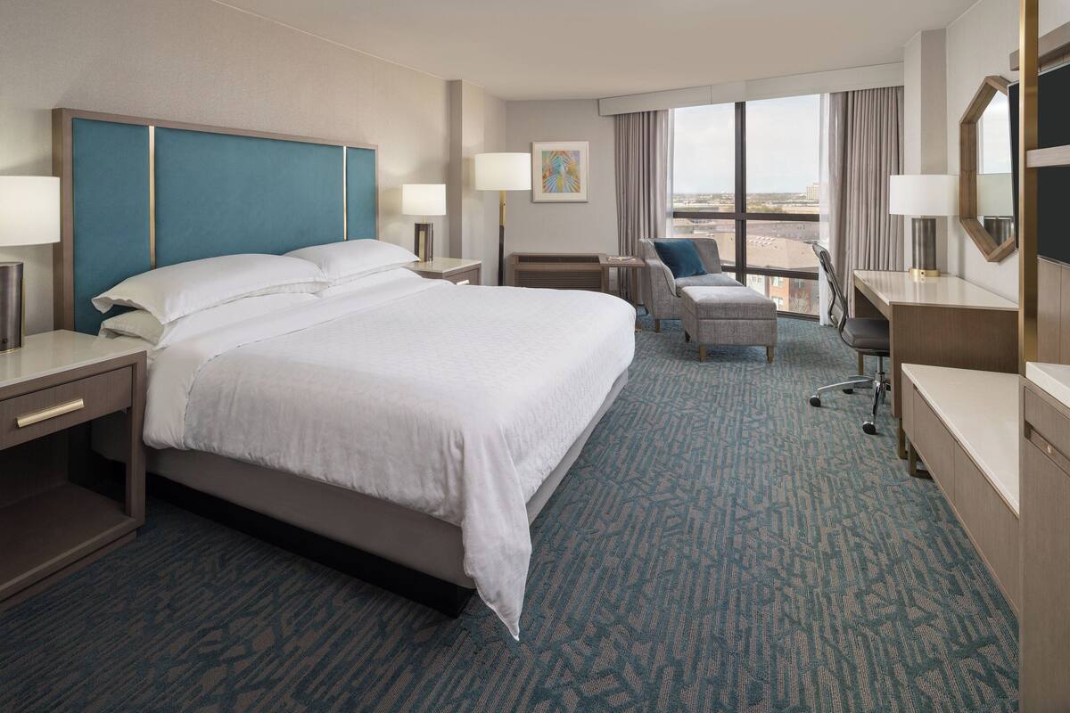 Habitación de hotel con una cama grande, un escritorio, una silla y vistas a la ciudad.