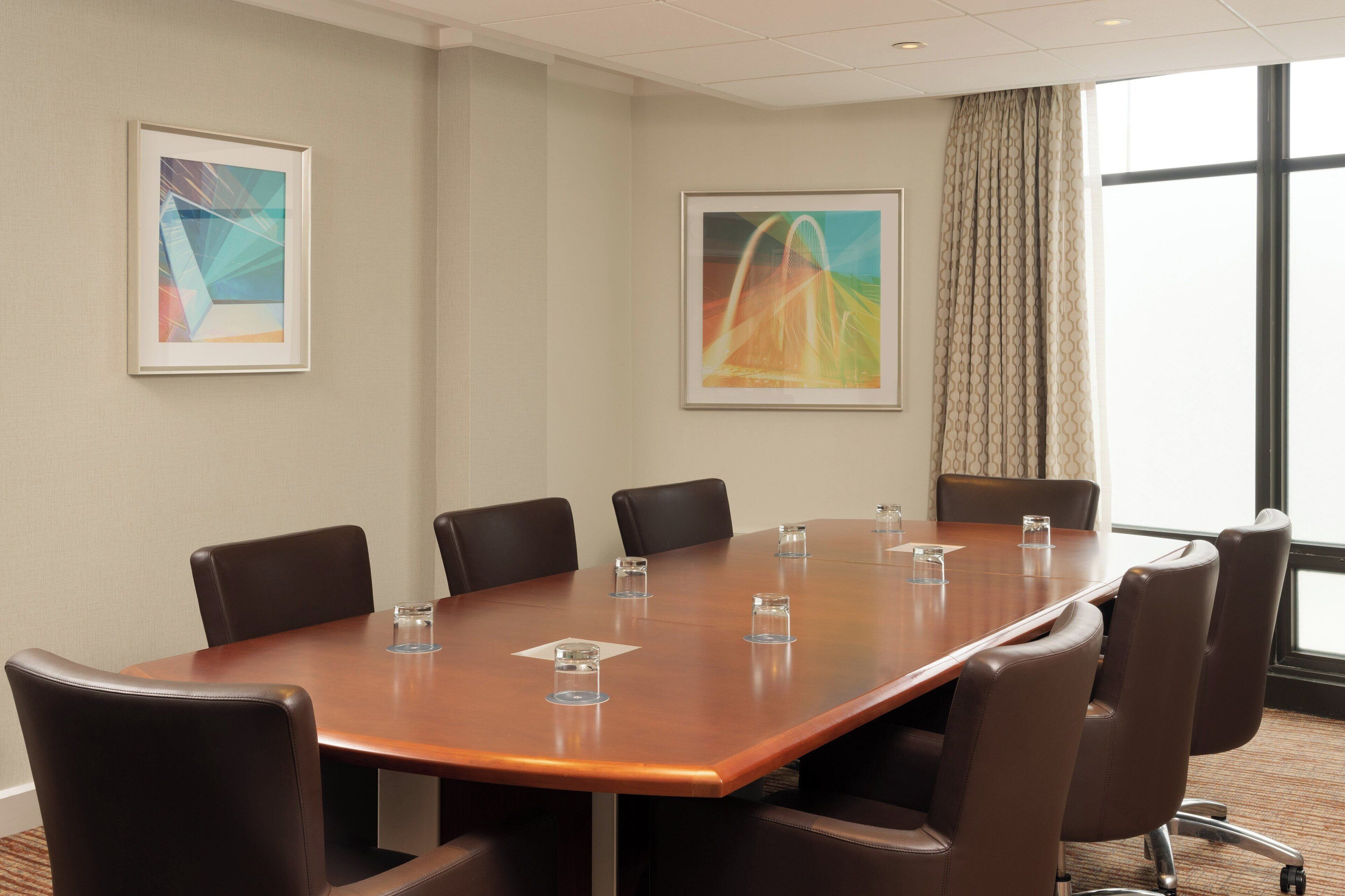 A conference room with a long table, eight chairs, and two framed abstract paintings on the walls.