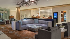 A modern hotel lobby with a sectional sofa, armchairs, a coffee table, and a decorative chandelier.