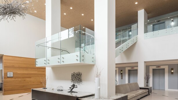 A modern lobby with a reception desk, seating area, glass railings, and a staircase.