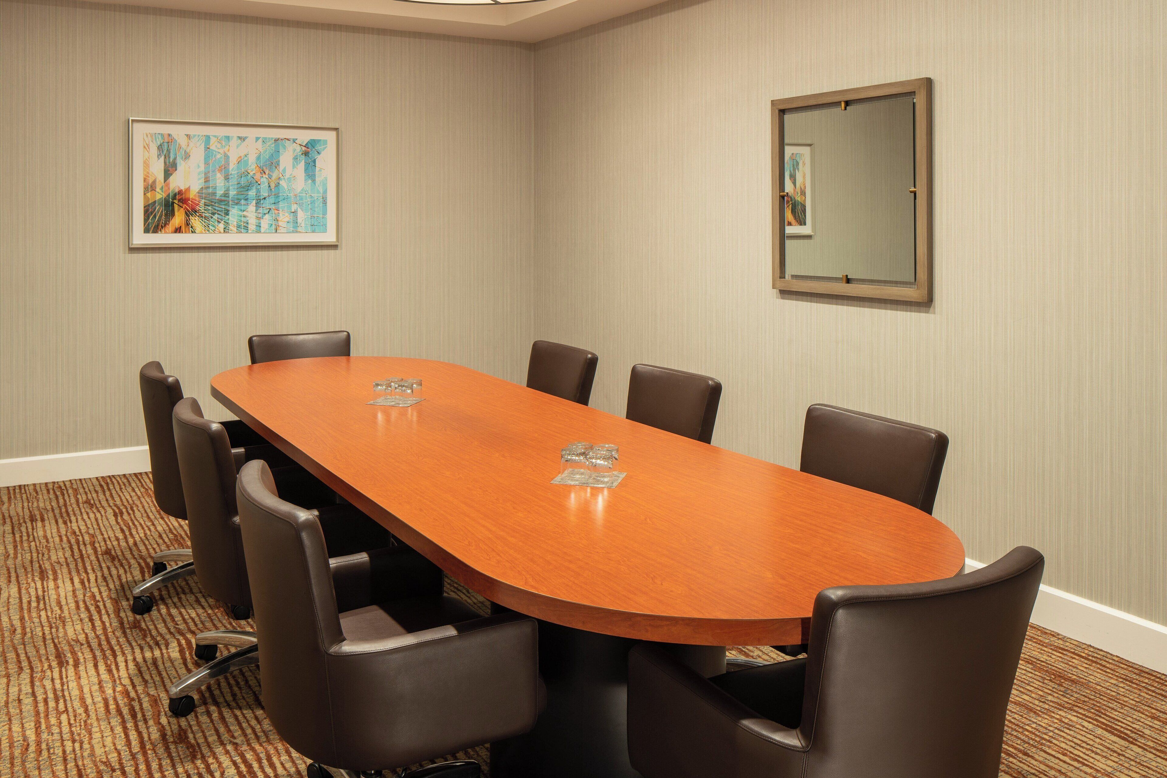 A conference room with a long wooden table, six black chairs, and two framed artworks on the walls.