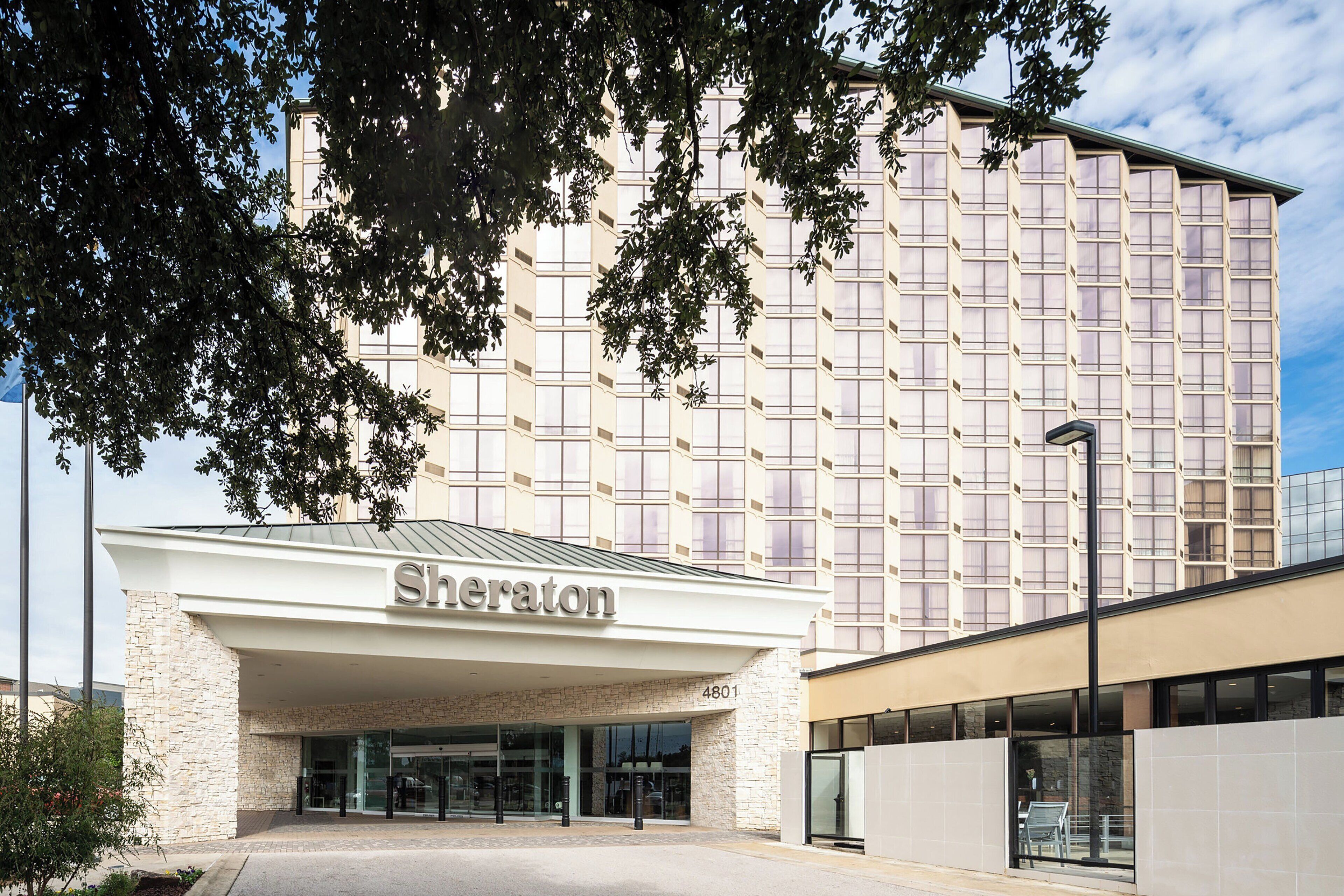 A Sheraton hotel entrance with a modern facade, large windows, and a stone base.