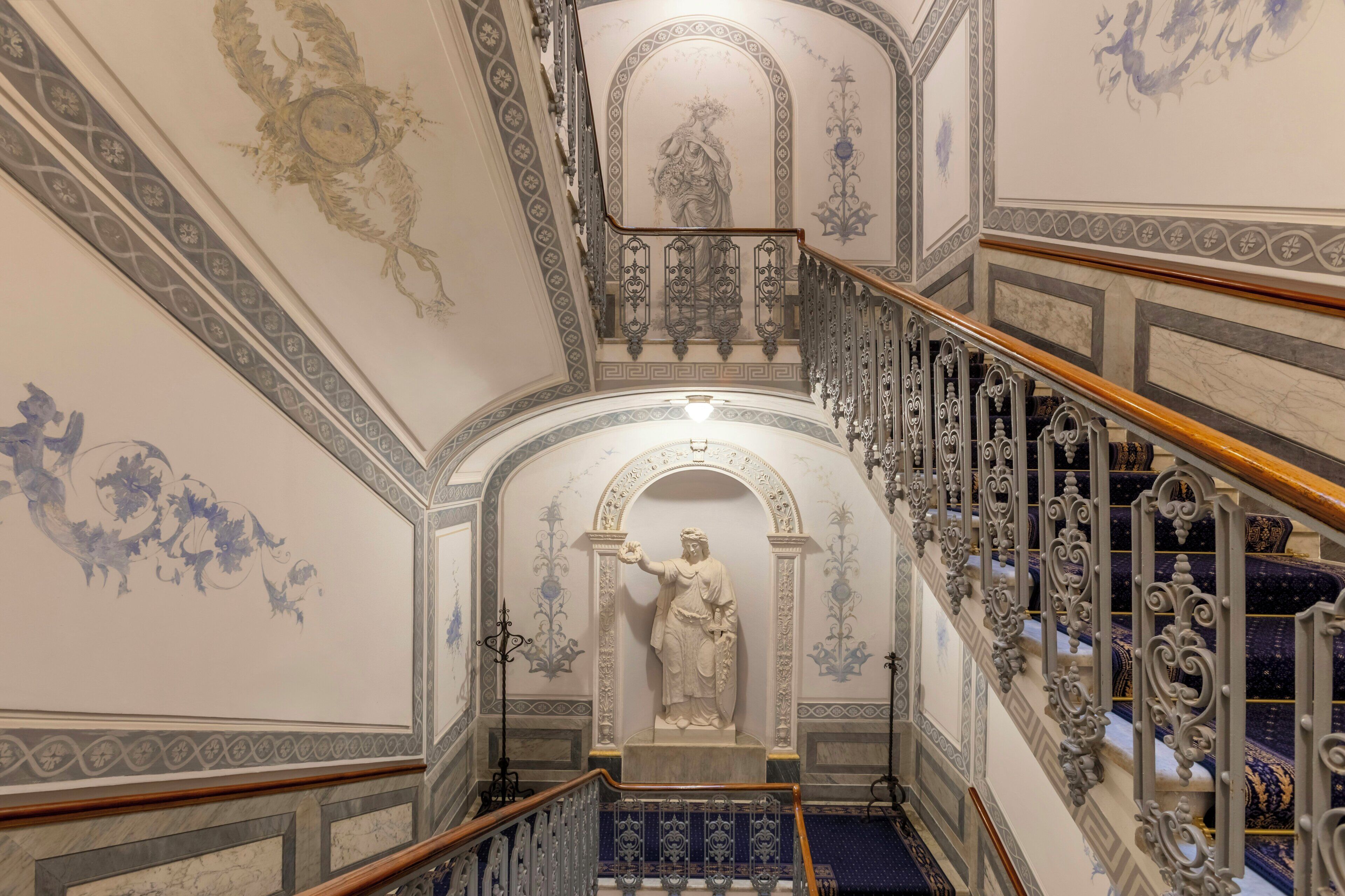 Eine prachtvolle Treppe mit aufwendiger Balustrade und einer Statue am oberen Ende.