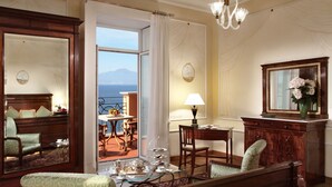 Una habitación con vista al mar, un rincón de comedor con una mesa dispuesta para el té y un espejo grande con un jarrón de flores.