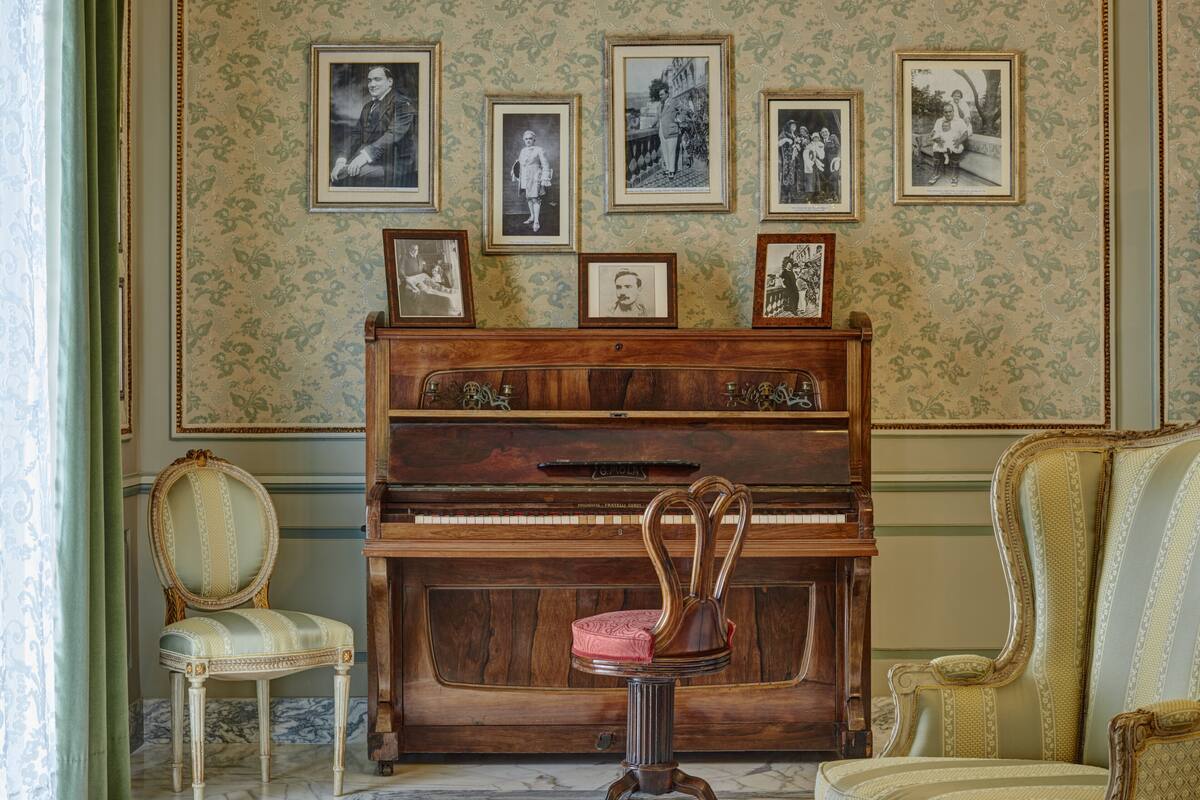 Una habitación con un piano de cola, una silla con cojín y una pared decorada con cuadros.