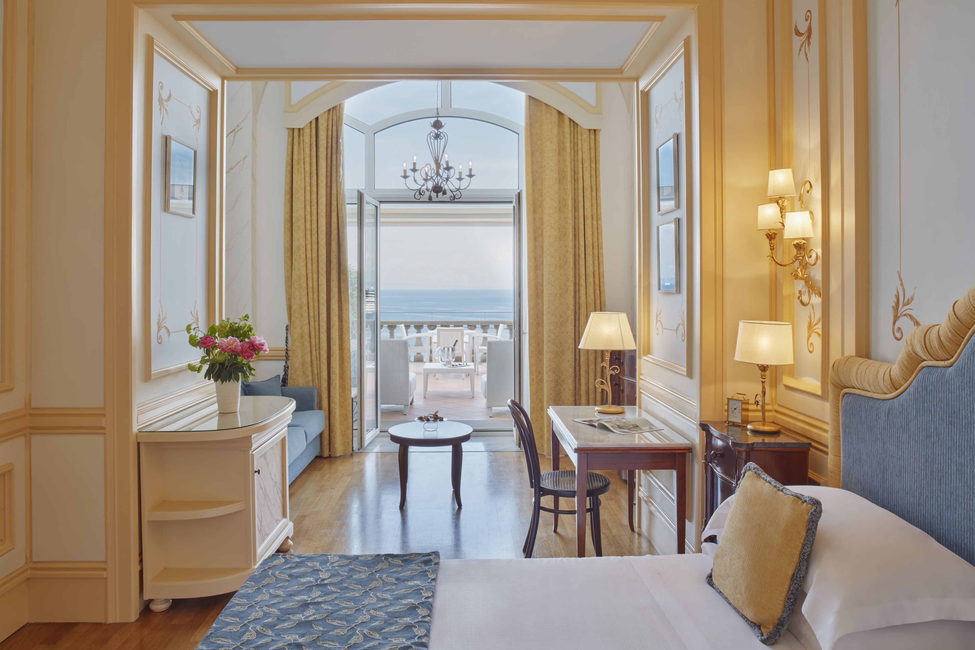 Camera d'albergo con un letto, una scrivania, una sedia, un tavolo e vista sul mare attraverso una porta aperta.