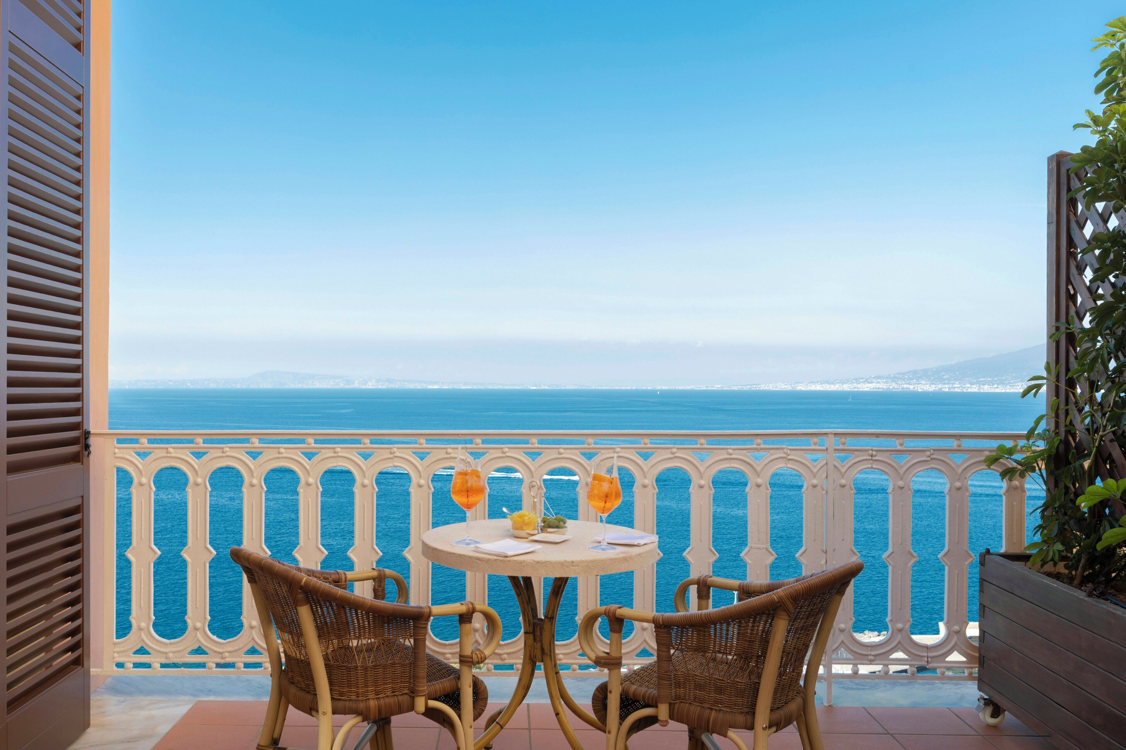 Un balcón con sillas de mimbre y una mesa, con vistas a la costa.