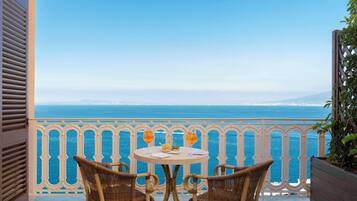 Un balcón con sillas de mimbre y una mesa, con vistas a la costa.
