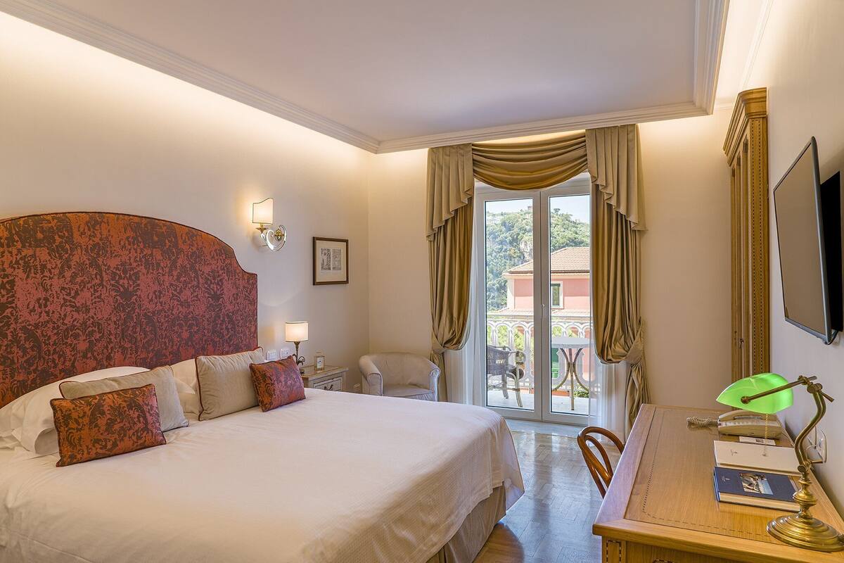 Habitación de hotel con una cama grande, un escritorio con lámpara, una silla y vistas al exterior a través de un ventanal.