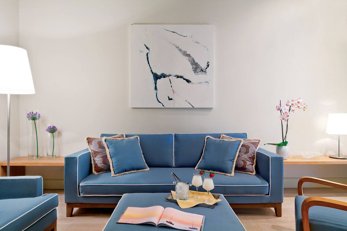 Una sala de estar moderna con un sofá azul, una mesa de centro con un libro y bebidas, y un cuadro en la pared.