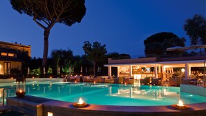 Un espace piscine doté d’un bar, de chaises longues et d’un grand arbre.