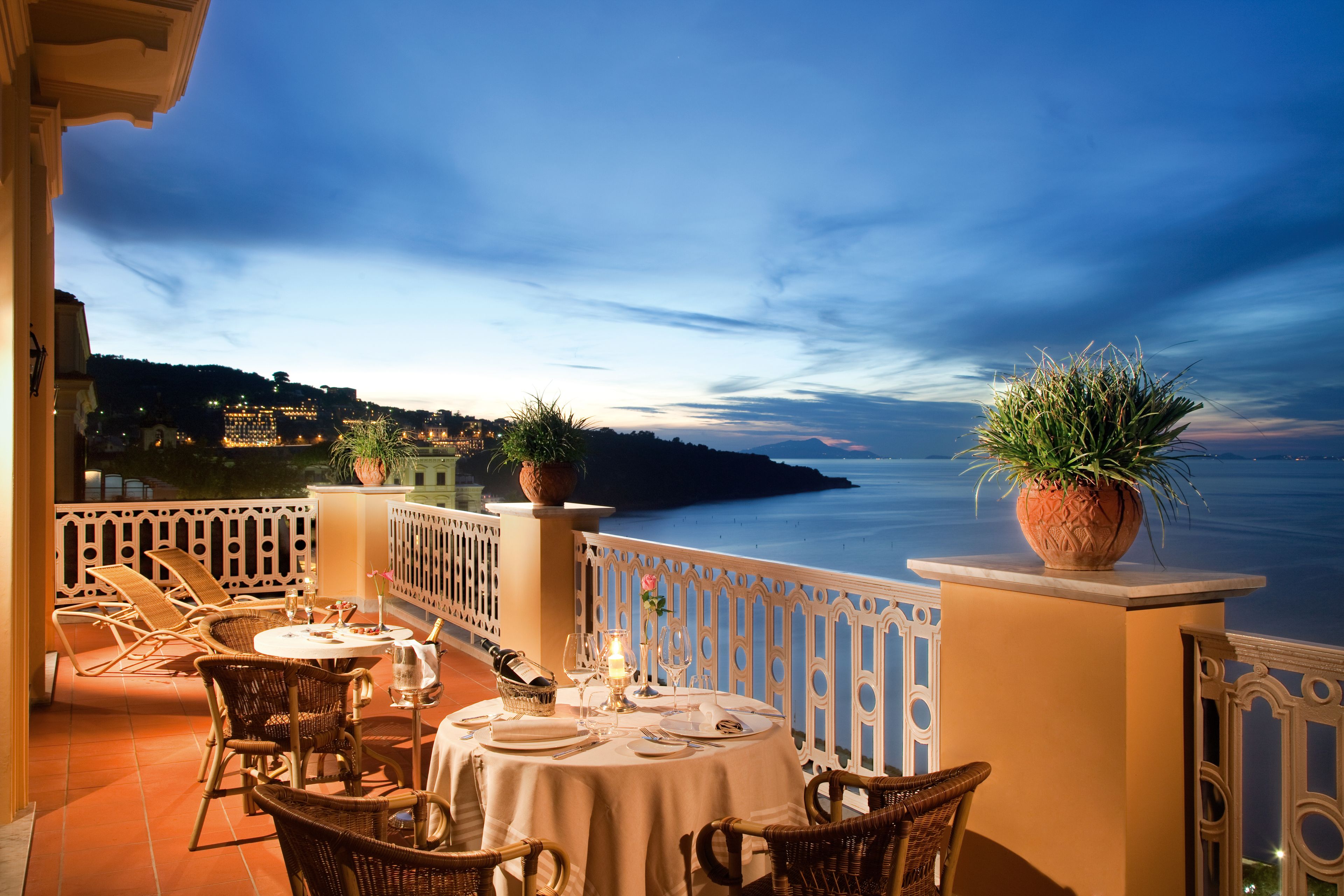 A terrace with wicker furniture, a table set for dining, and potted plants.