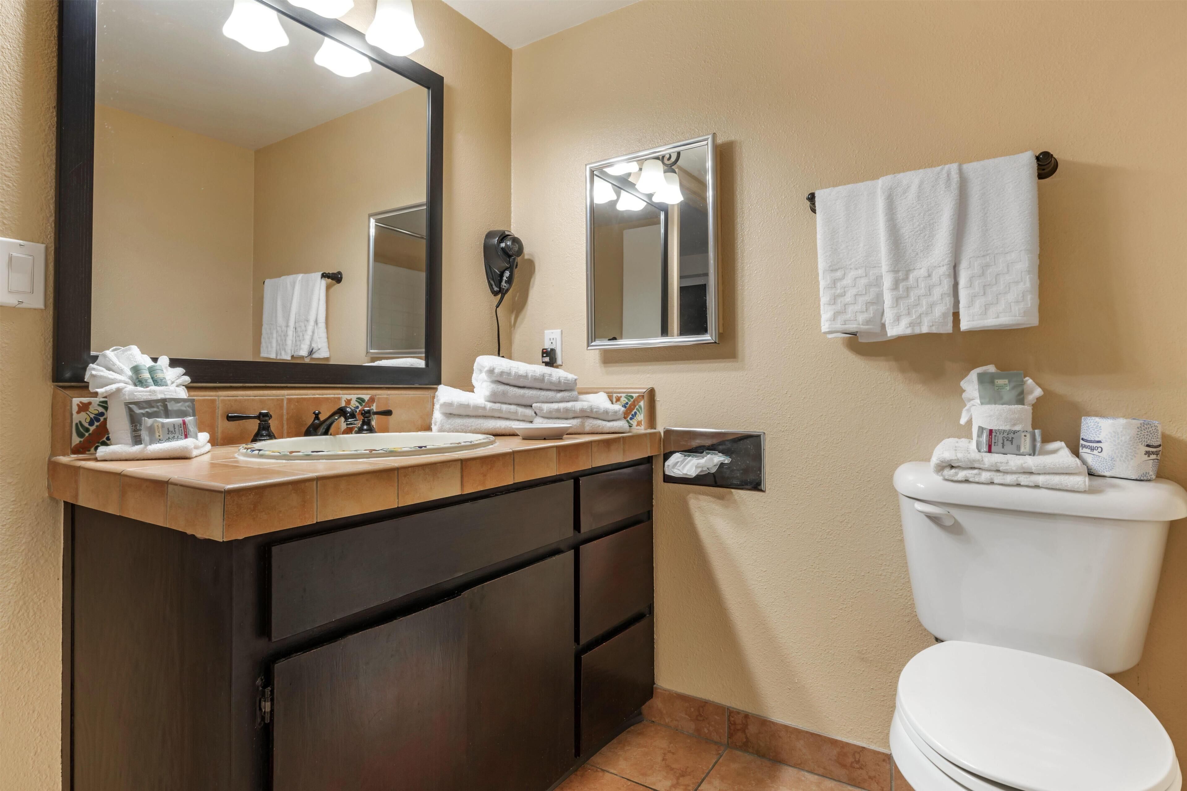 A bathroom with a wooden vanity, a large mirror, a toilet, and a towel rack.