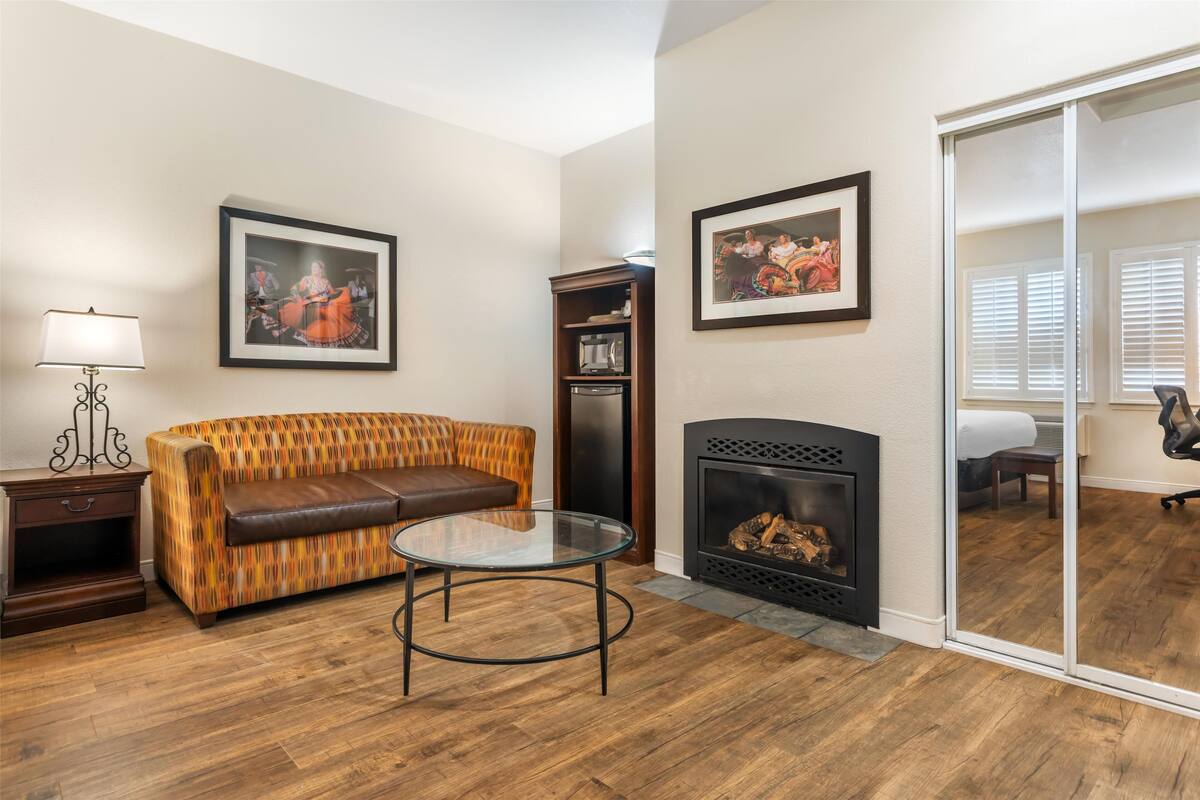 A living room with a patterned sofa, a glass coffee table, a fireplace, and two framed pictures on the wall.