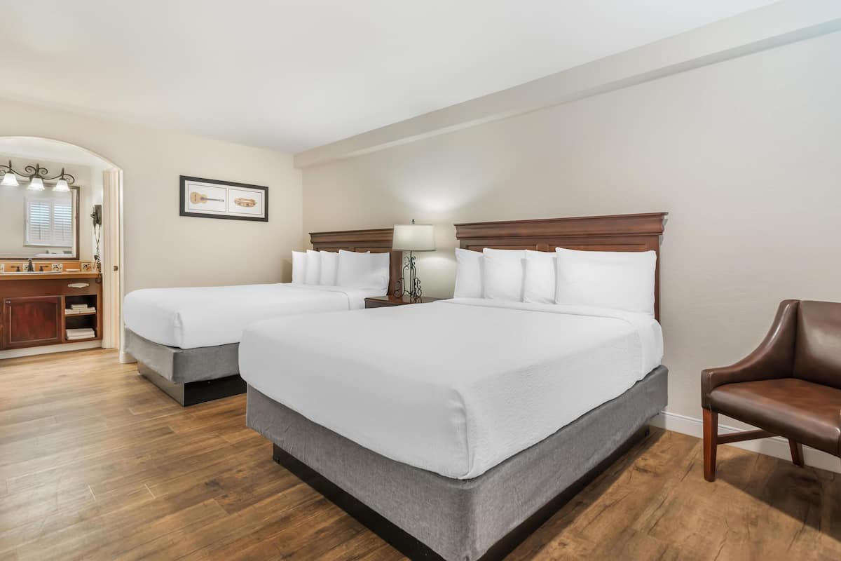 A hotel room with two single beds, a wooden floor, a desk with a mirror, and a brown leather chair.