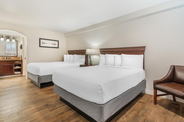 A hotel room with two single beds, a wooden floor, a desk with a mirror, and a brown leather chair. - Best Western Rose Garden Inn (Watsonville)