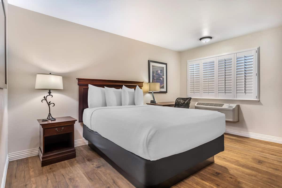 A hotel room with a large bed, a nightstand with a lamp, a framed picture on the wall, and an air conditioning unit.