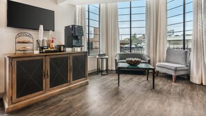 A modern living room with a flat-screen TV, a coffee machine, and a dining area with stacked plates and cups. - Best Western Rose Garden Inn (Watsonville)