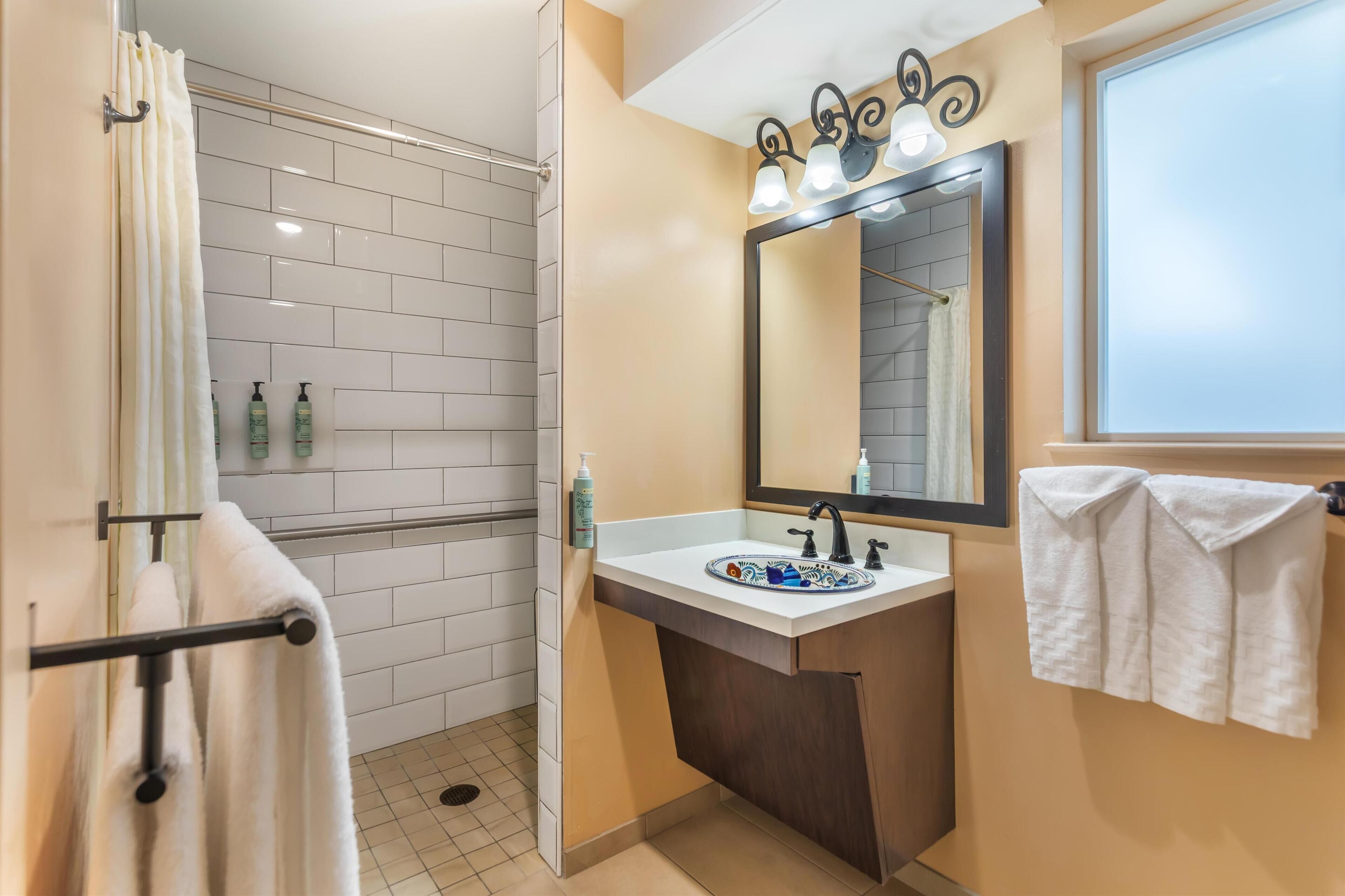 A bathroom with a shower, a sink with a mirror, and towels hanging on a rack.