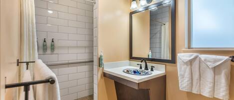 A bathroom with a shower, a sink with a mirror, and towels hanging on a rack.