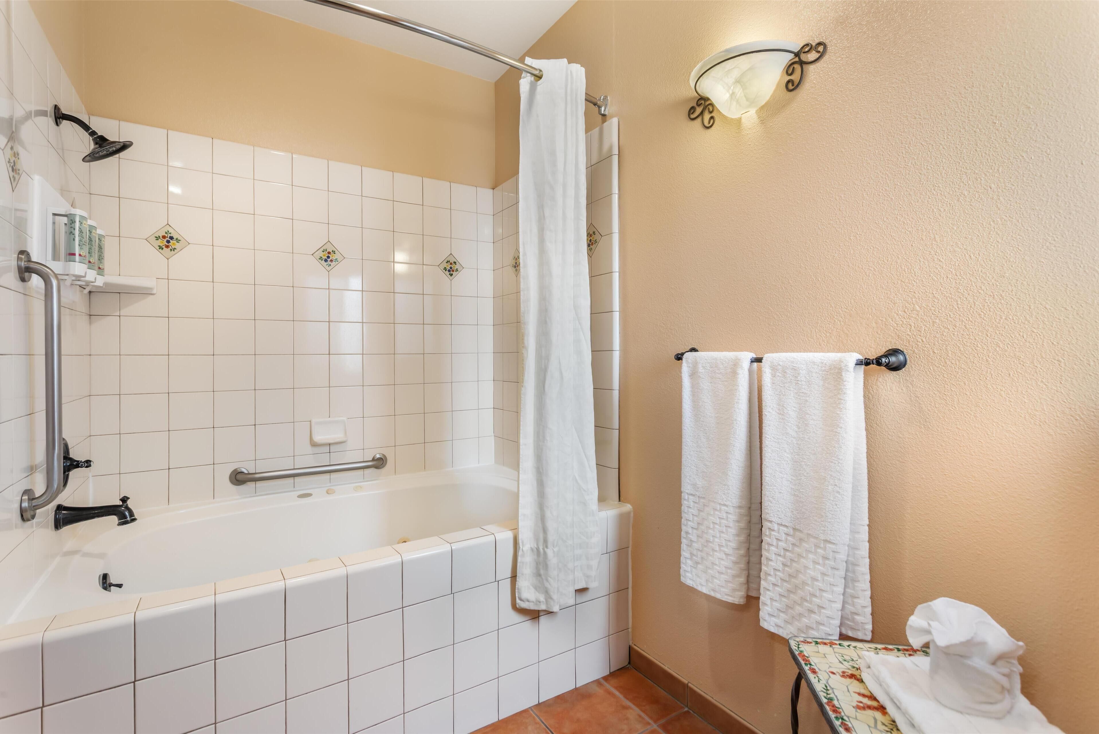 A bathroom with a bathtub, a shower, a towel rack, and a small table with a towel.