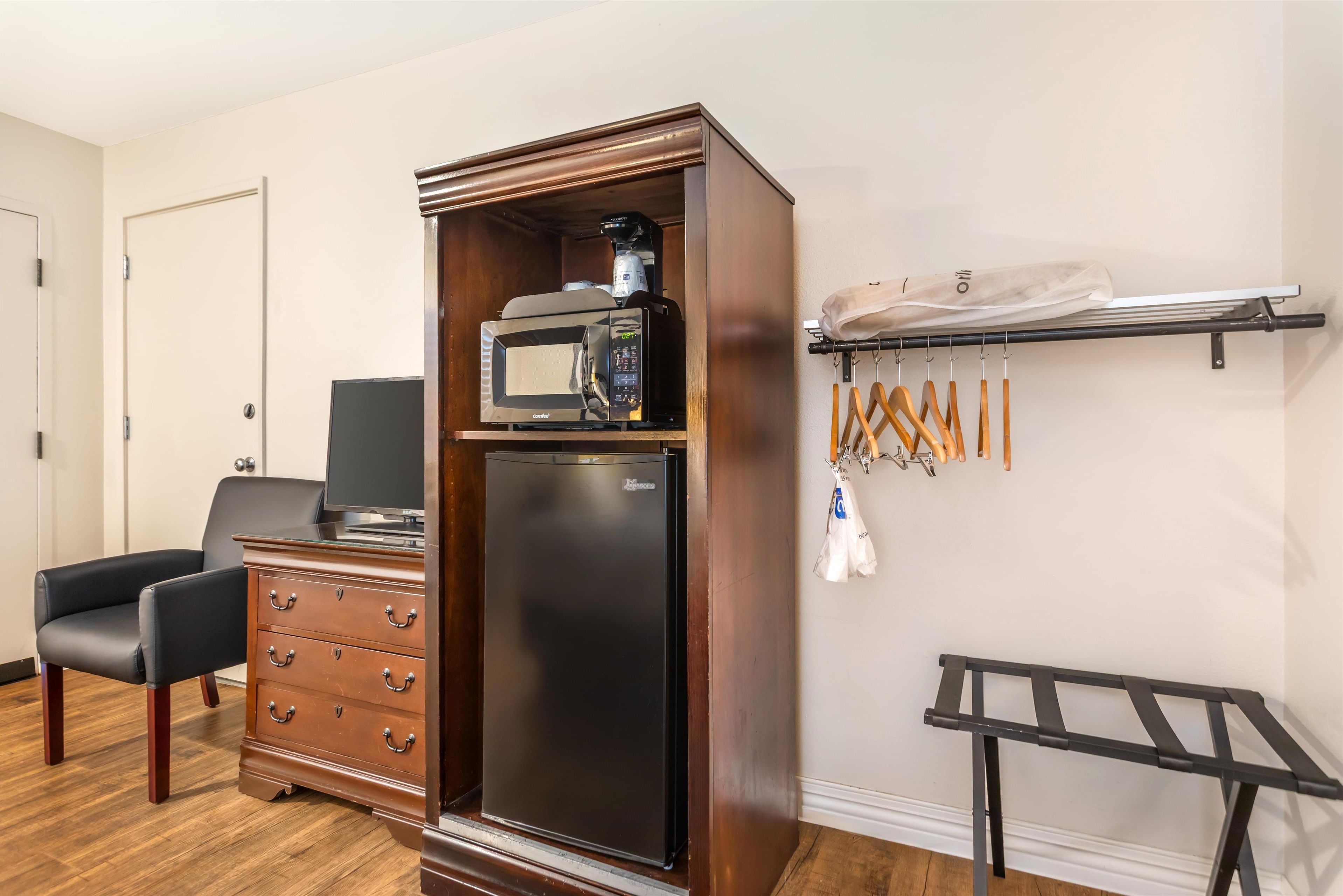 A compact kitchenette with a microwave, coffee maker, and refrigerator, a wooden dresser, a chair, and a drying rack.