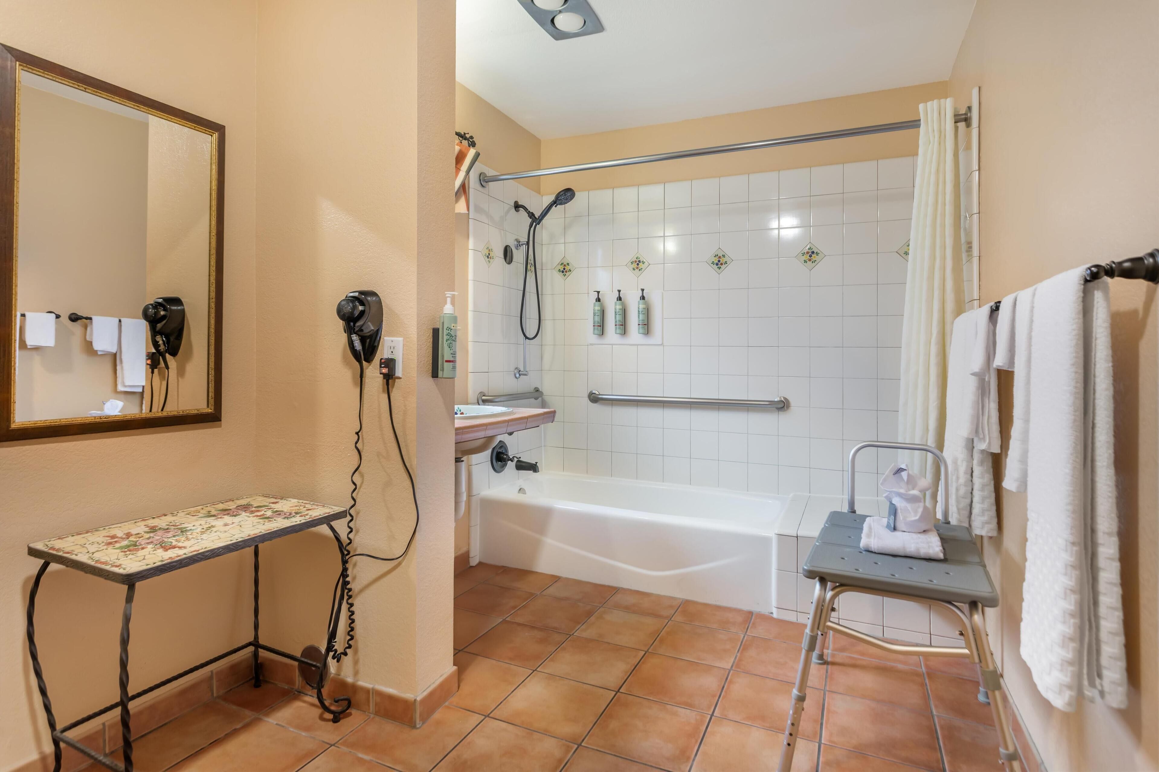 A bathroom with a shower, a sink, a mirror, and a small table.