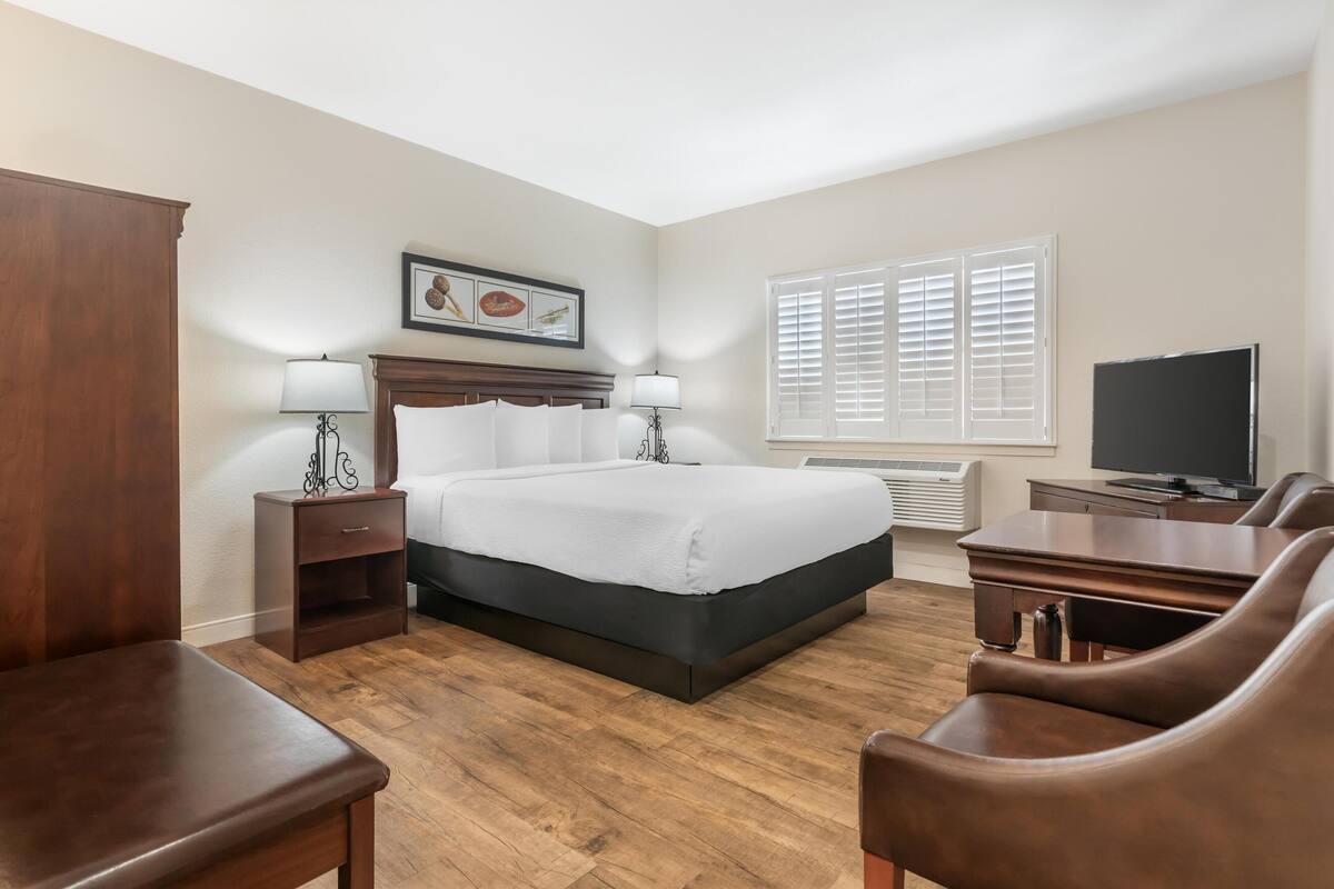 A hotel room with a bed, two bedside tables with lamps, a TV, a desk, and a chair.