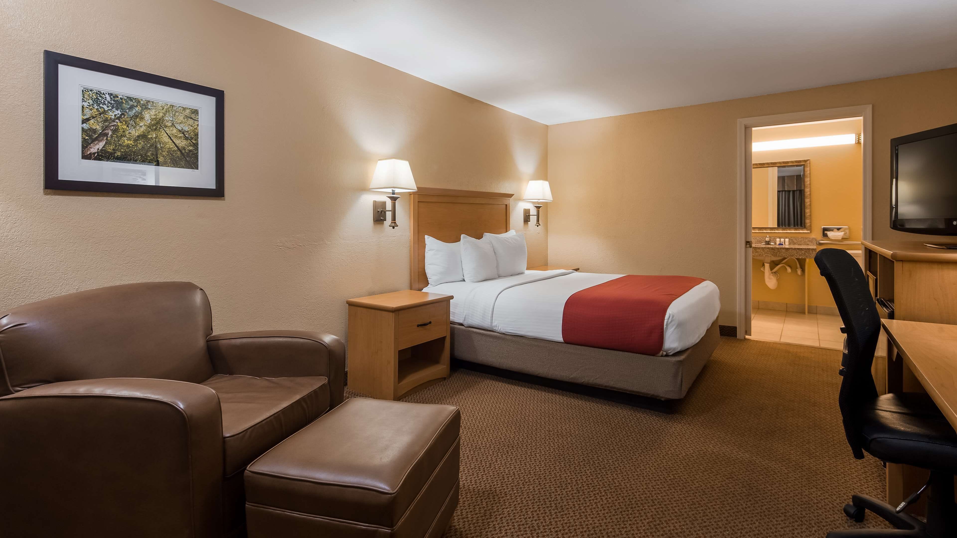 Habitación de hotel con cama, escritorio, silla, mesita de noche y televisor.