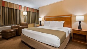 Una habitación de hotel con una cama grande, dos mesitas de noche, una silla, un escritorio y un ventanal con cortinas.
