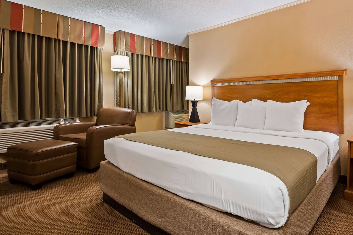 A hotel room with a large bed, two bedside tables, a chair, a desk, and a large window with curtains.