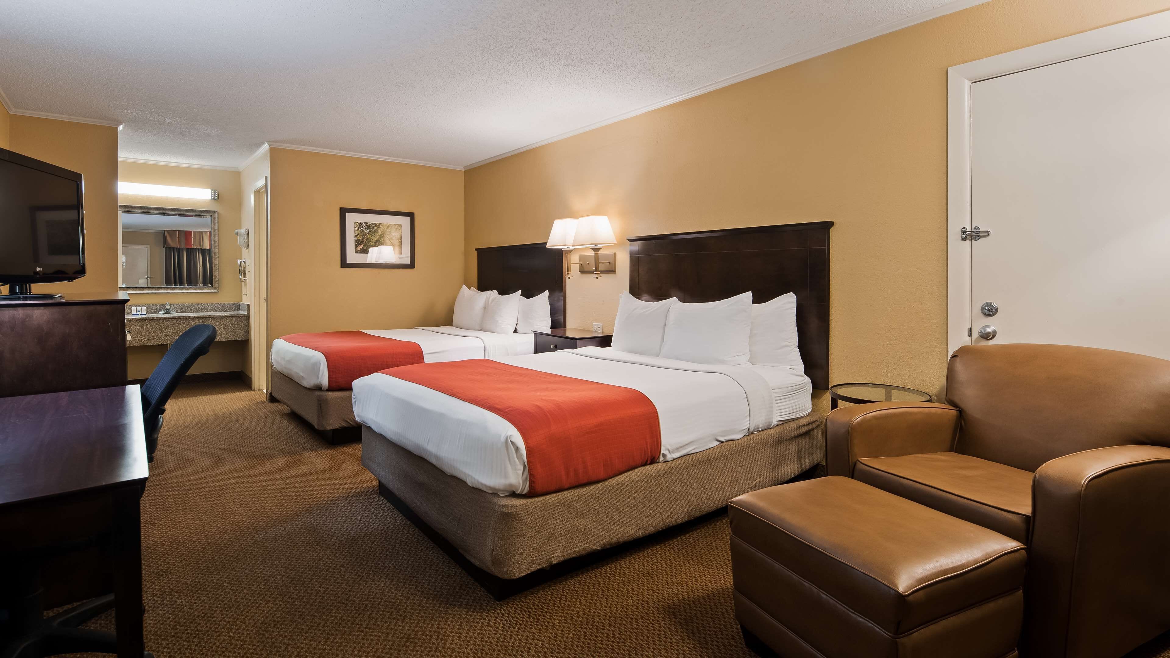 A hotel room with two beds, a desk, a chair, and a television.