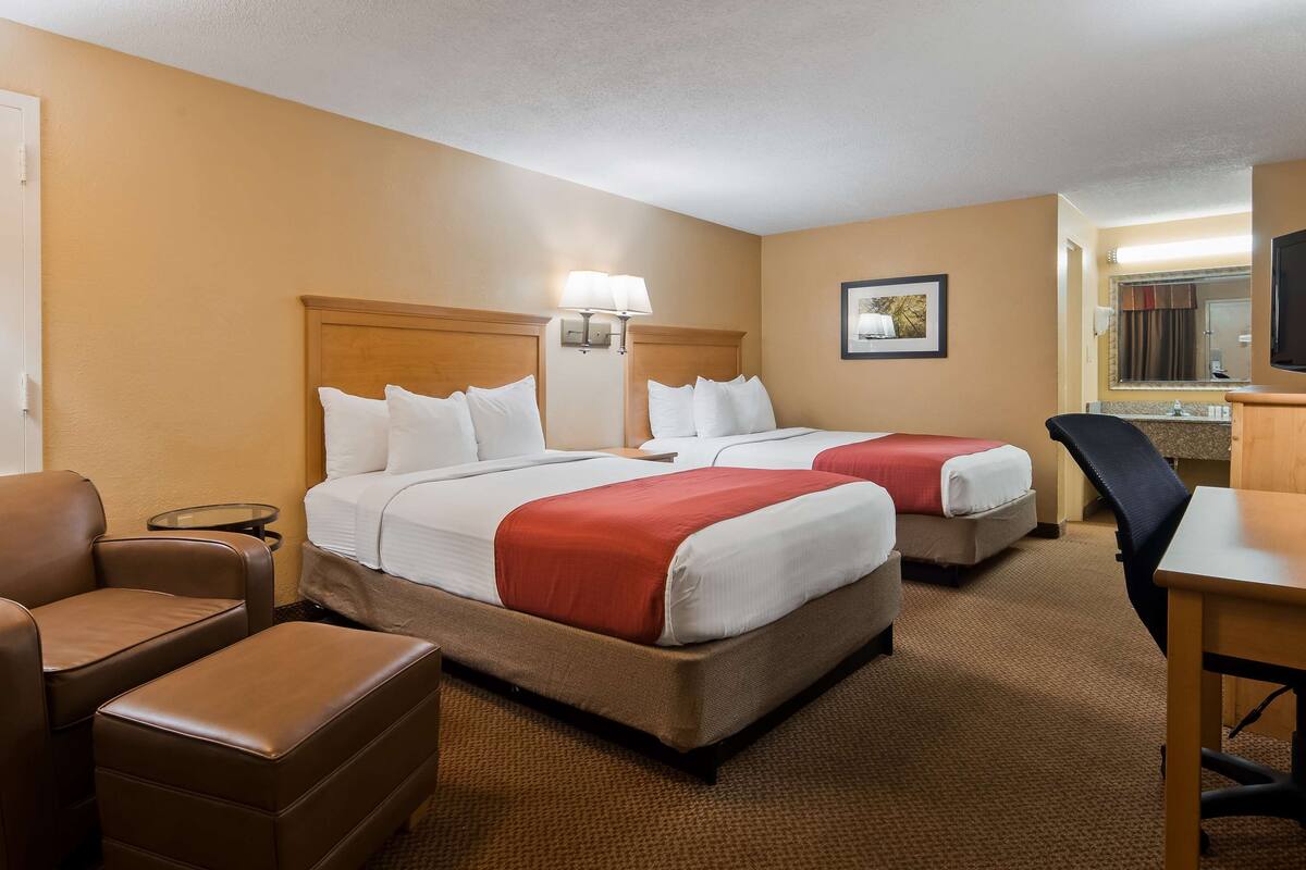 A hotel room with two beds, a desk, a chair, and a small table.