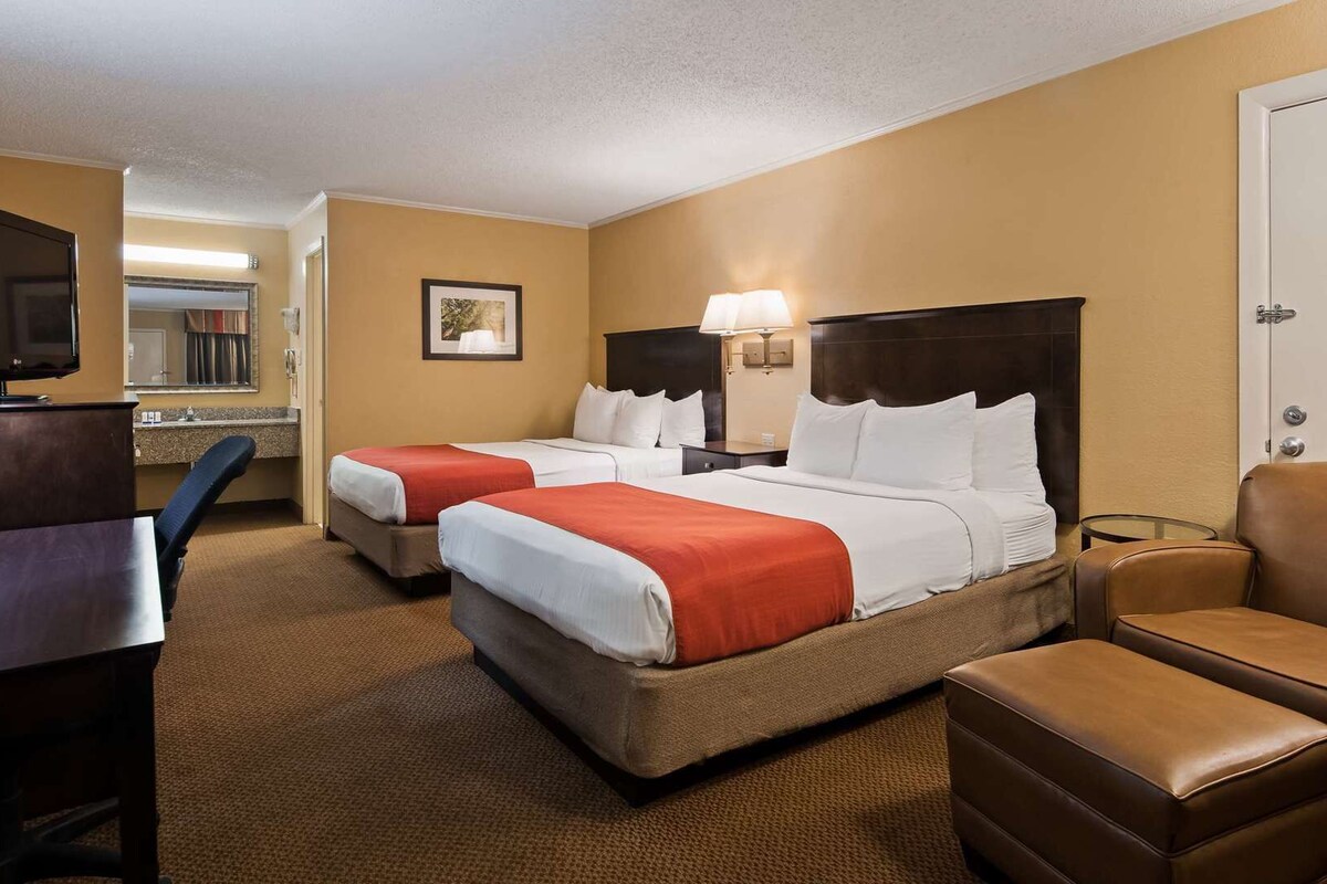 A hotel room with two beds, a desk, a chair, and a television.