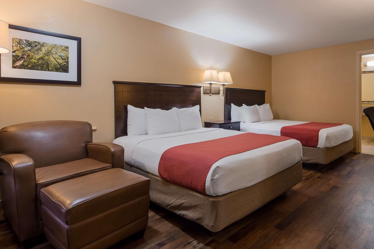 A hotel room with two beds, a brown leather chair, a desk, and a television.