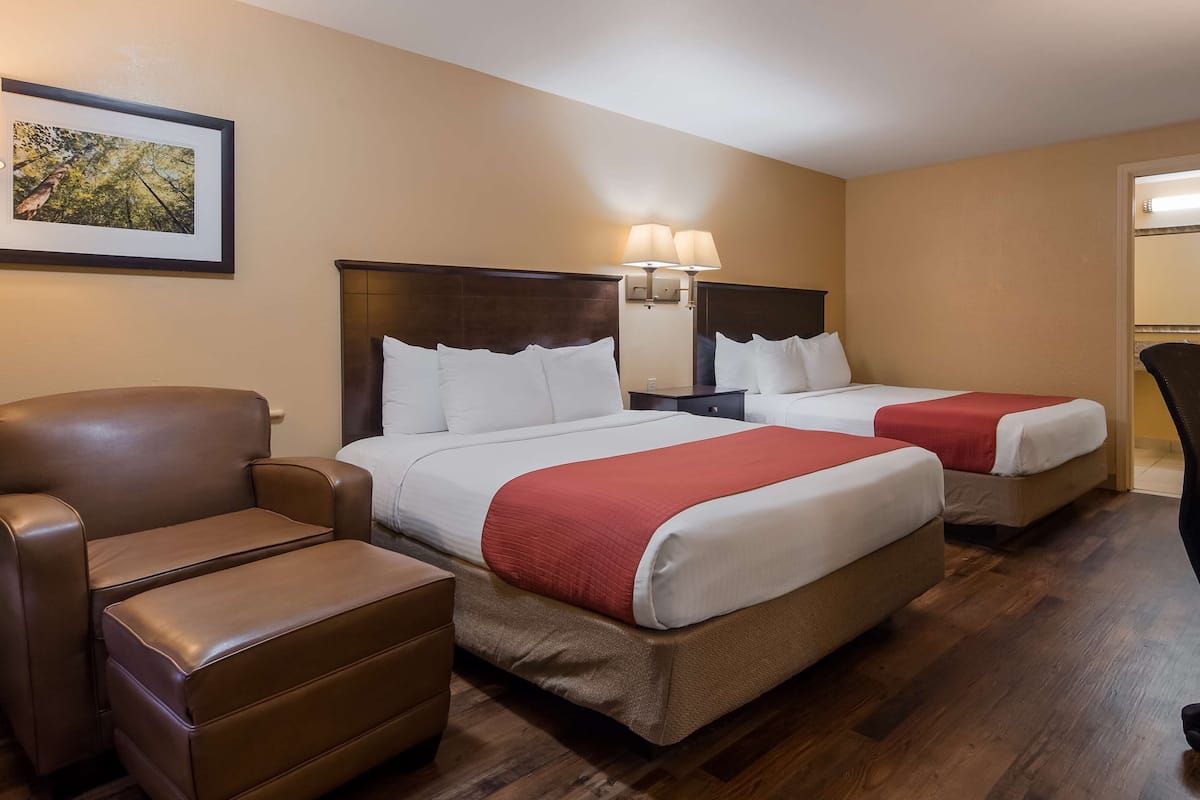 A hotel room with two beds, a desk, a chair, a sofa, and a framed picture on the wall.
