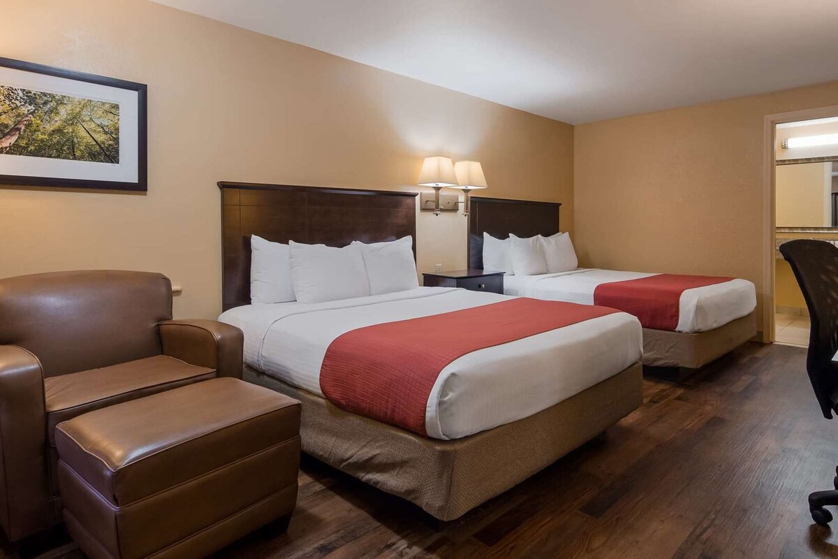 A hotel room with two beds, a desk, a chair, a lamp, and a framed picture on the wall.