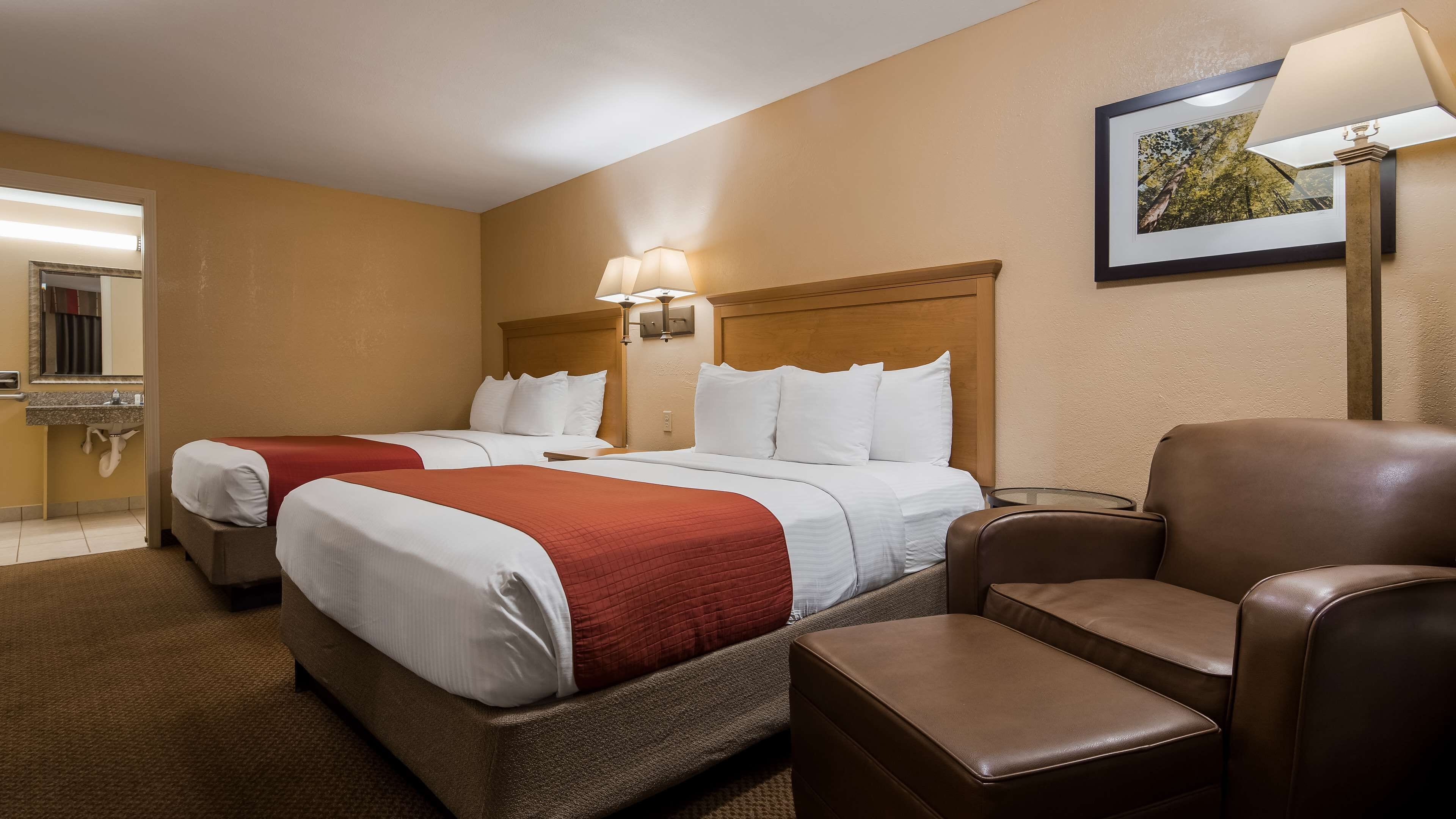 A hotel room with two beds, a sitting area, a small table, and a framed picture on the wall.