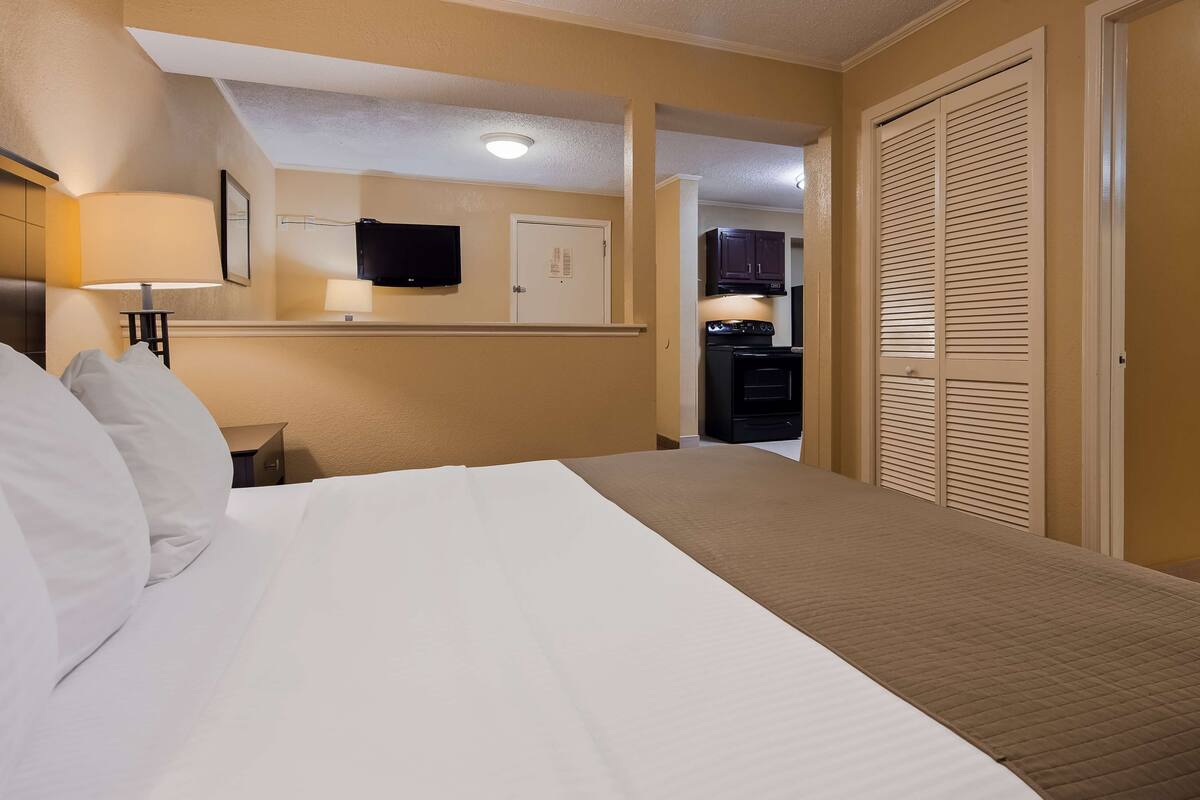 A hotel room with a bed, a TV, a desk with a lamp, a wardrobe, and a bathroom visible through an open door.