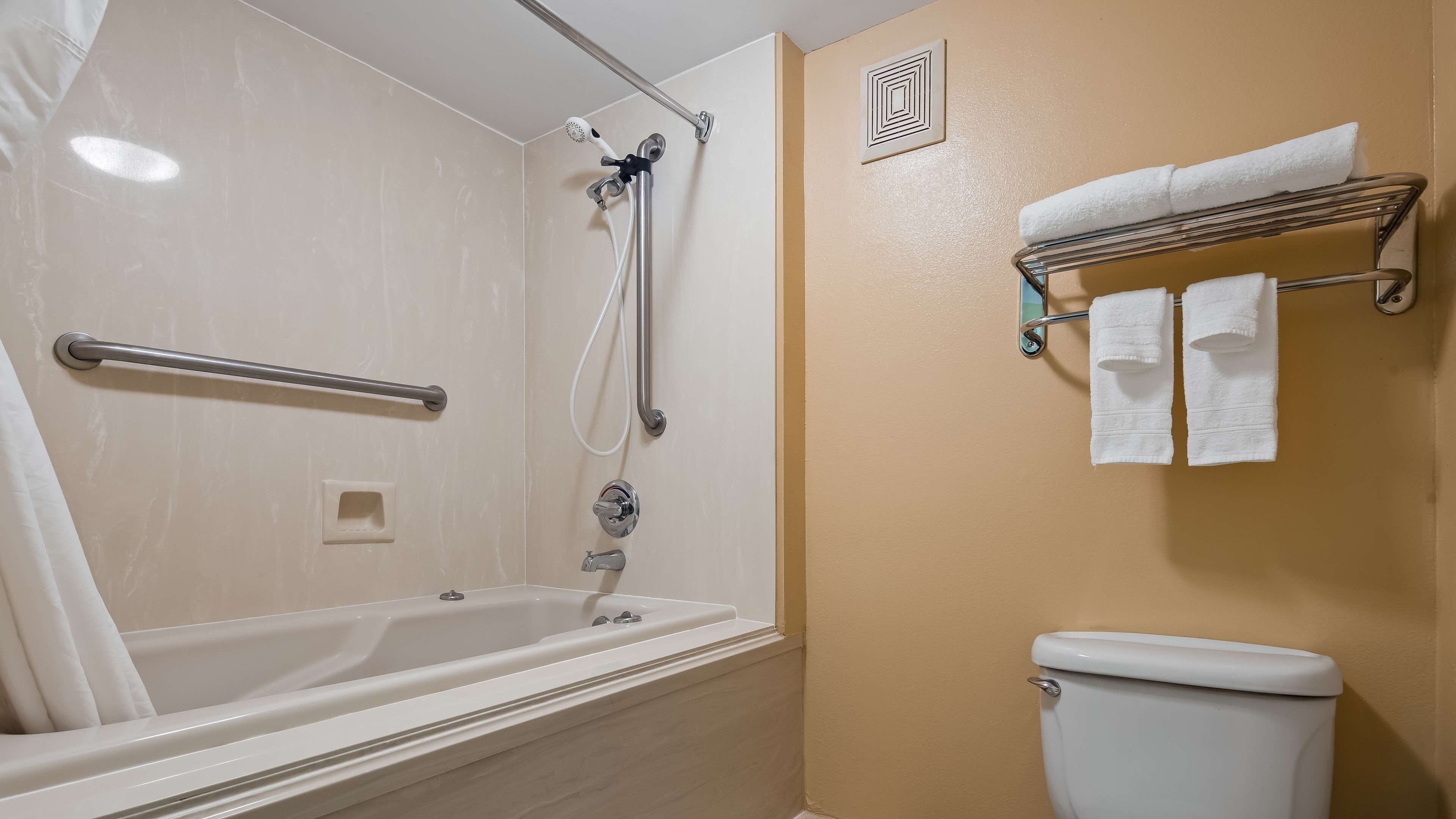Et badeværelse med badekar, bruser og toilet. Der er en håndklædestang med håndklæder og et gelænder.