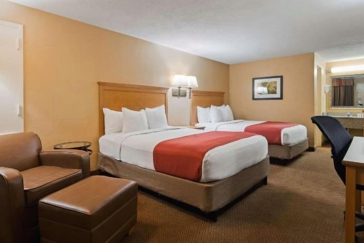 A hotel room with two beds, a desk, a chair, a lamp, and a television.