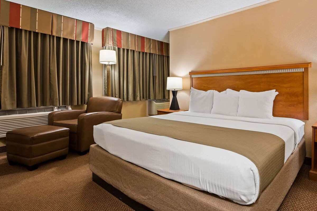 A hotel room with a large bed, two bedside tables, a desk, a chair, and a window with curtains.