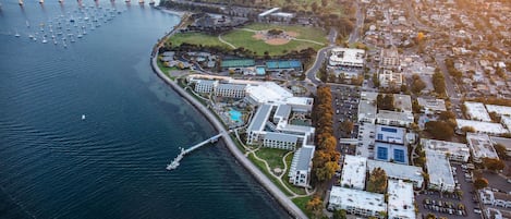 An aerial view of a coastal city with a marina, residential buildings, and a sports complex.