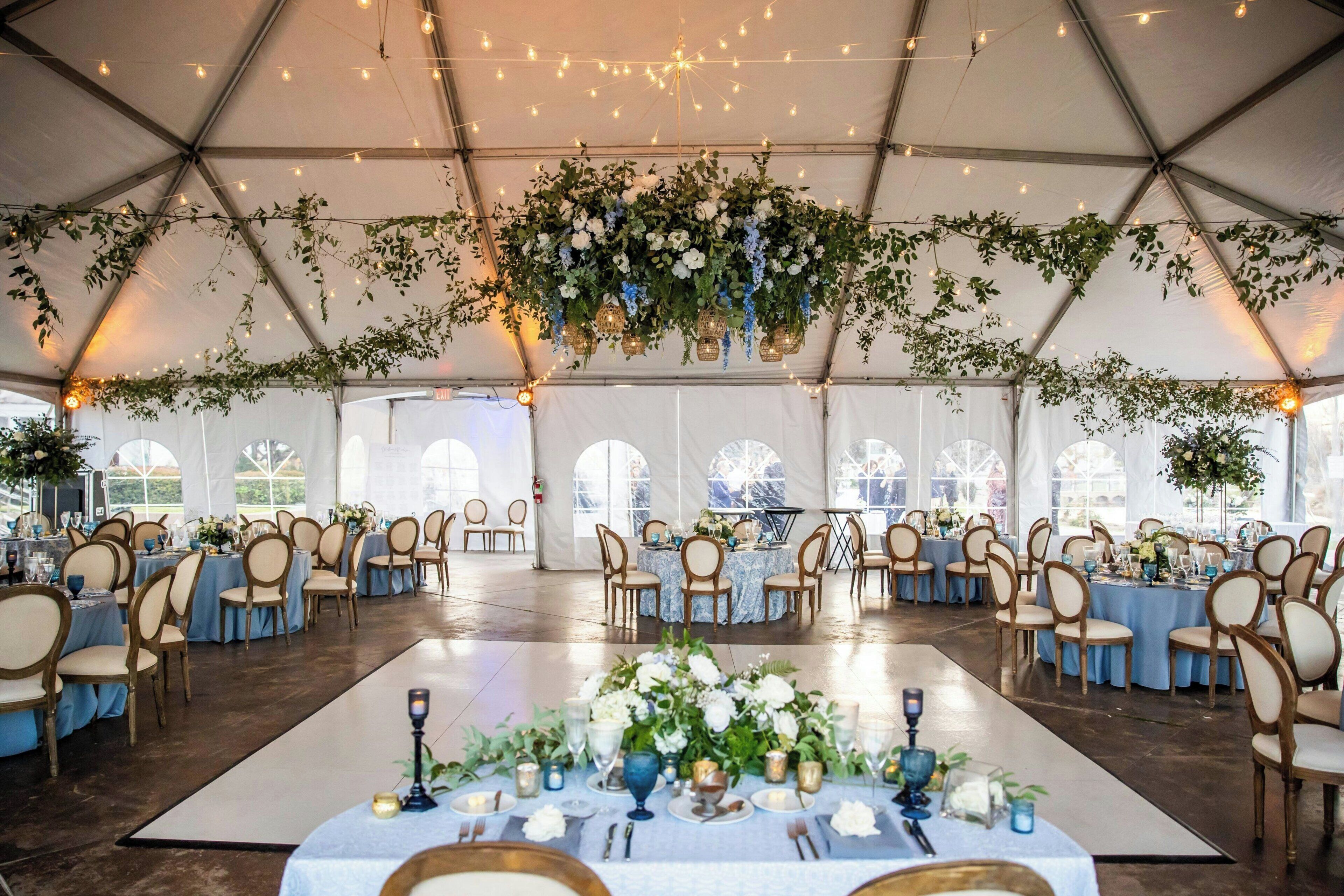 Un espace événementiel aménagé sous une tente, avec des tables rondes, des chaises et des décorations florales.
