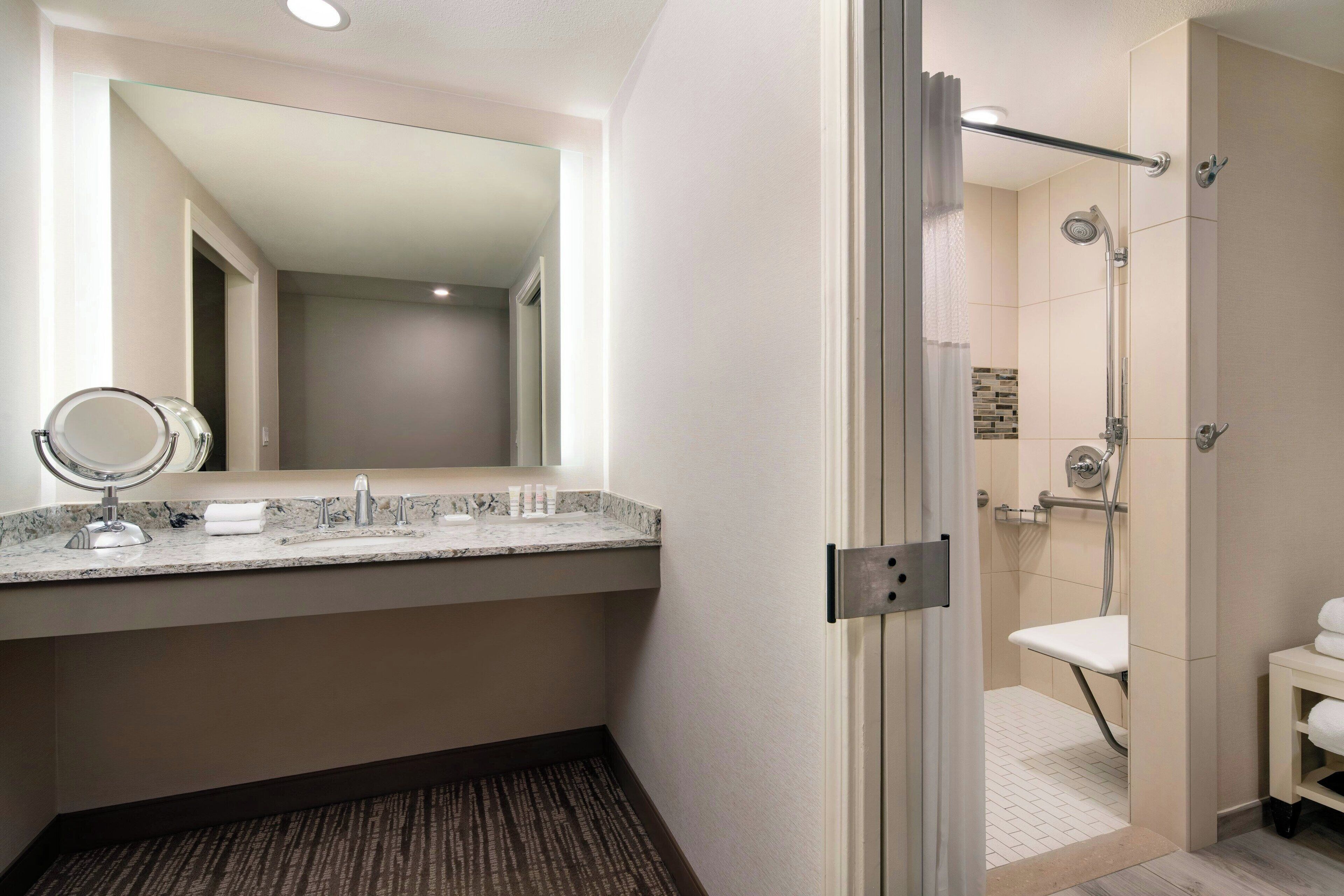 Une salle de bain moderne dotée d’un comptoir en granit, d’un grand miroir, d’une douche avec un pommeau de douche amovible et de toilettes.