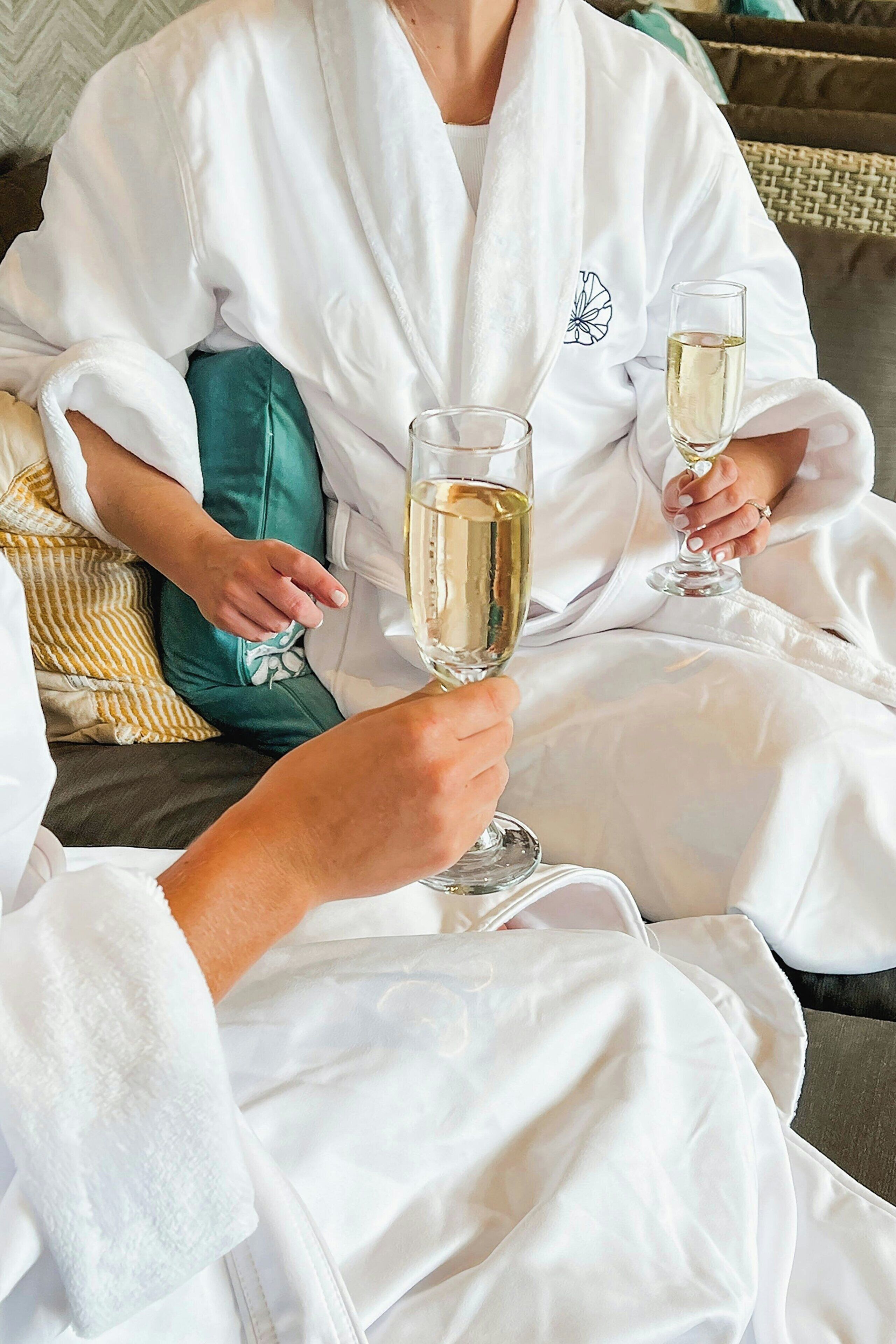 A person in a white robe sitting on a couch with a glass of champagne.
