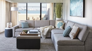 A living room with a large sectional sofa, a coffee table, and a view of the water and bridge. - Coronado Island Marriott Resort & Spa (Coronado)
