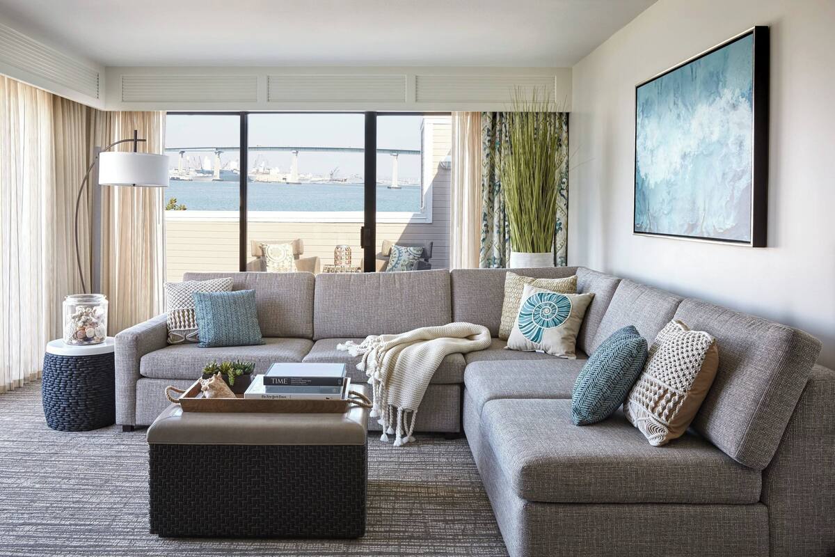 A living room with a large sectional sofa, a coffee table, and a view of the water and bridge.