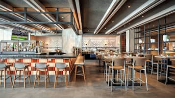 Un espace bar moderne avec des tabourets, un comptoir avec des bouteilles et un coin salon avec des tables et des chaises.