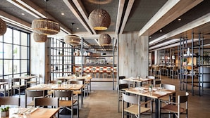 A spacious restaurant with high ceilings, exposed beams, and large windows. Tables are neatly arranged with chairs, and hanging wicker lamps provide lighting. - Coronado Island Marriott Resort & Spa (Coronado)